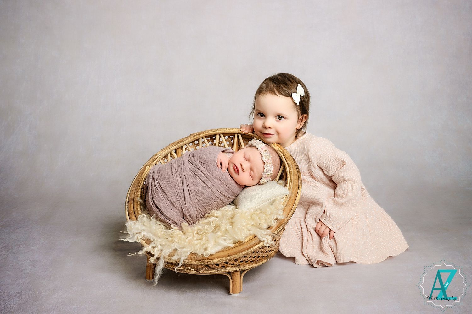 Sweet sibling moment with wicker basket against grey studio backdrop.