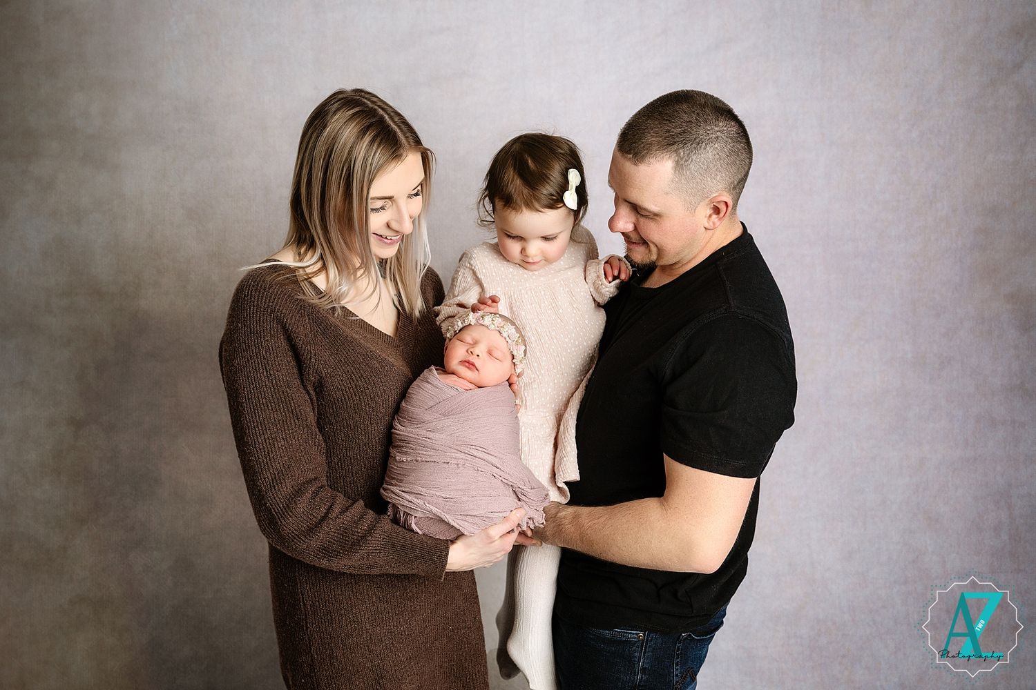 Candid moment of parents smiling at their baby while older sibling looks on.