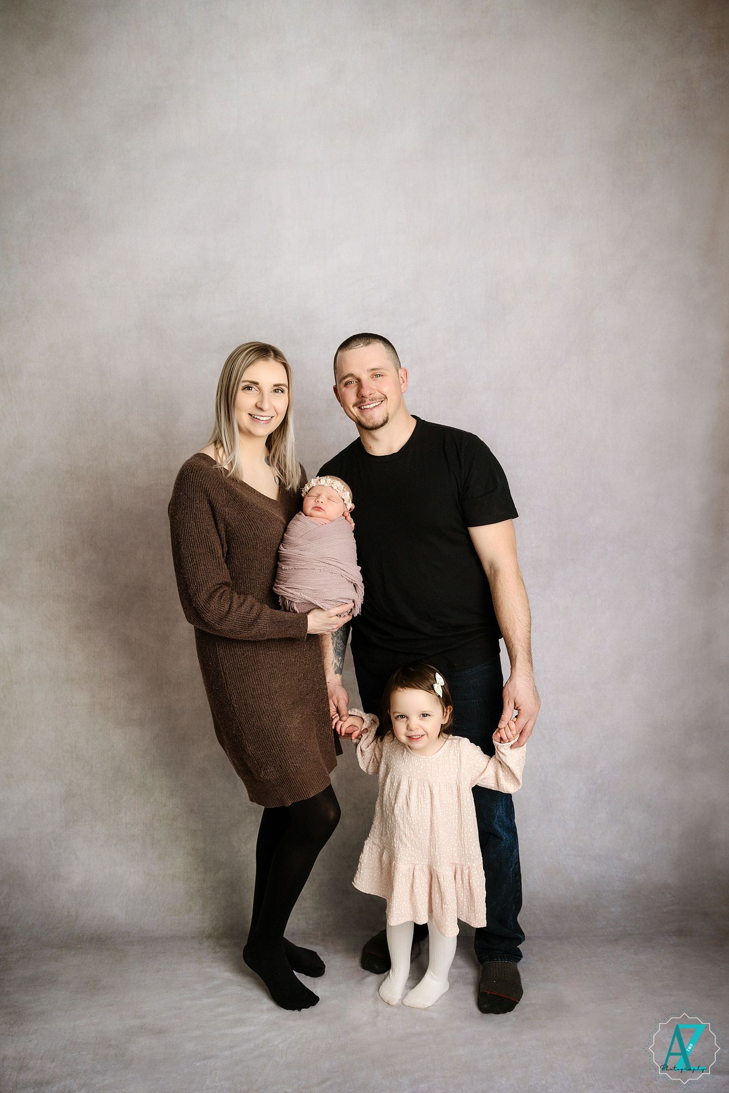 Full-length family portrait with parents and two children in coordinated brown and black outfits.