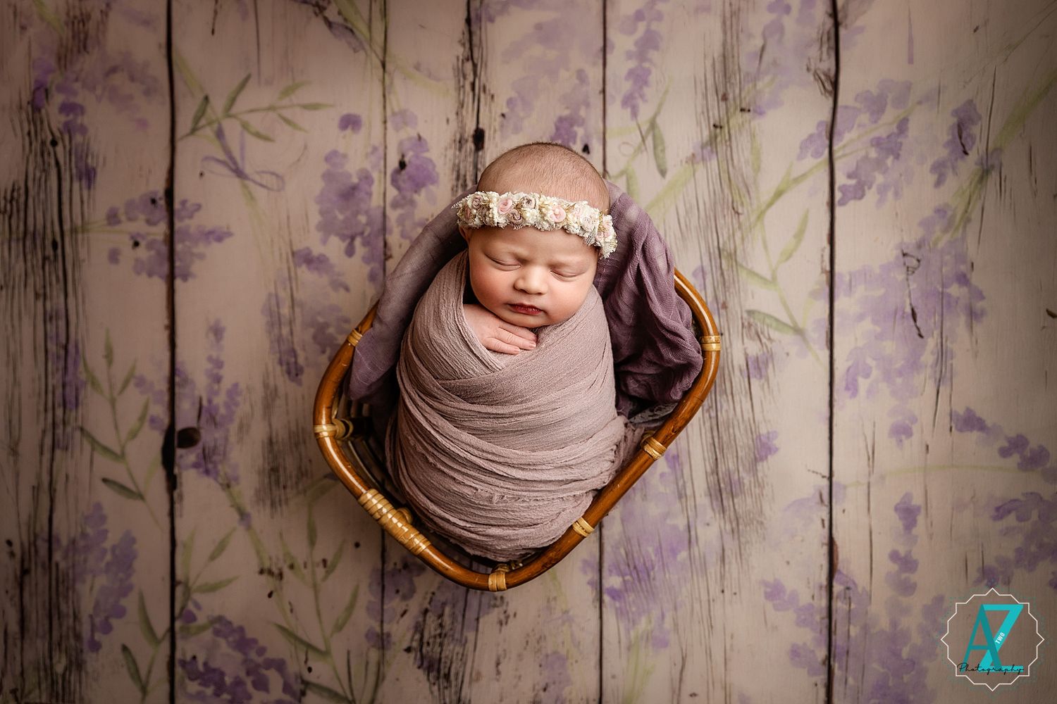 Overhead view of sleeping newborn in basket against purple floral backdrop.
