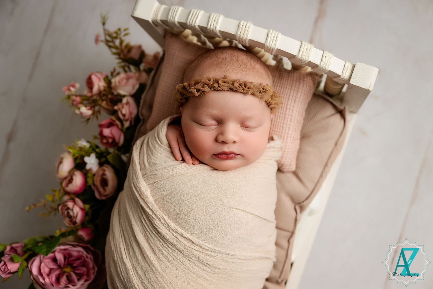 Newborn photography featuring soft blush pink flowers and delicate cream wrapping in an artistic studio setup.