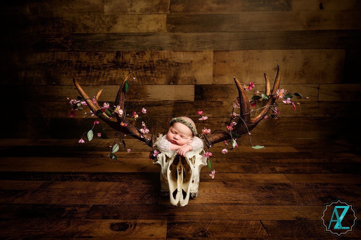 Creative newborn photo with decorated animal skull and floral arrangement on dark wooden background.