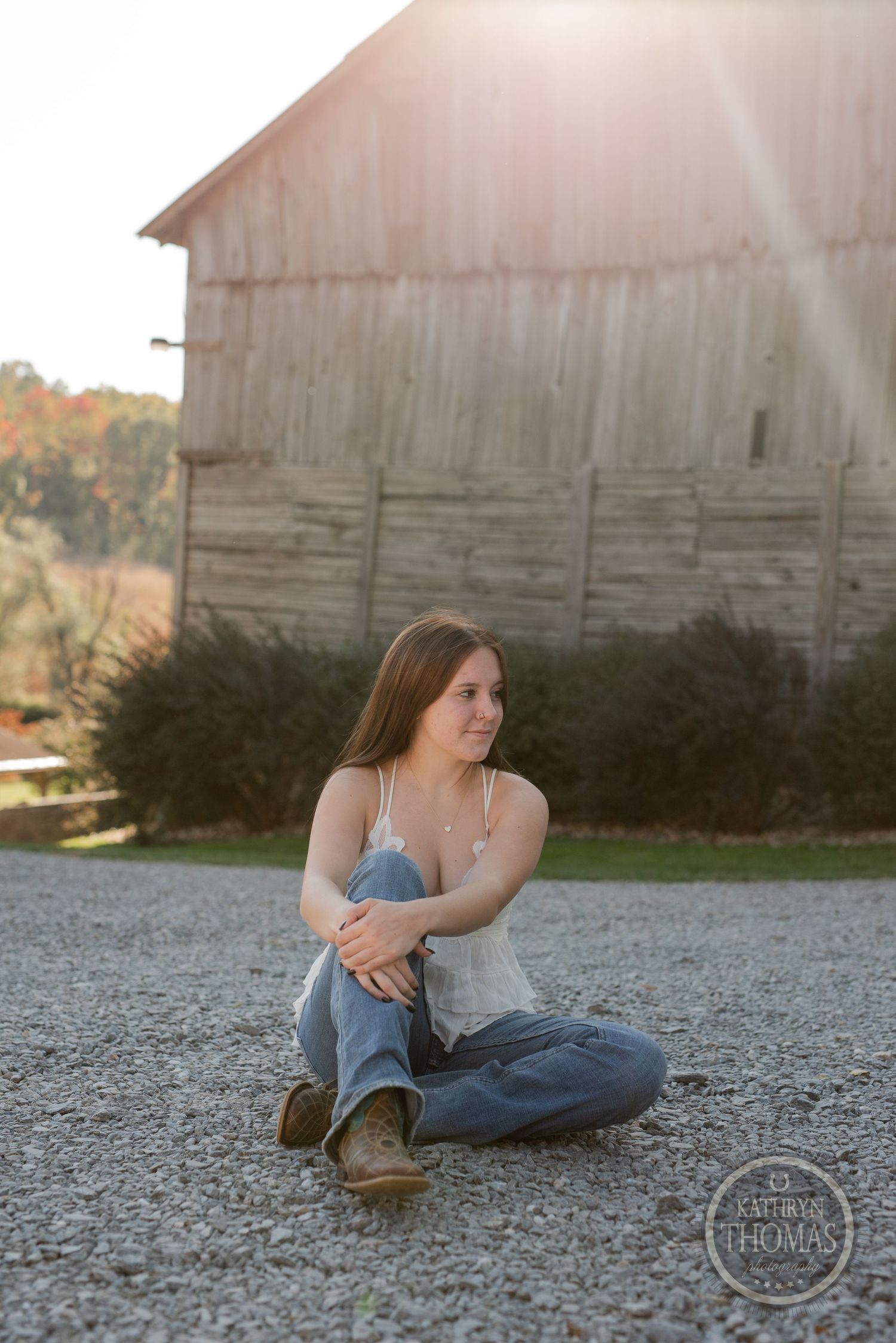 Casual outdoor portrait sitting on gravel with rustic barn in background.