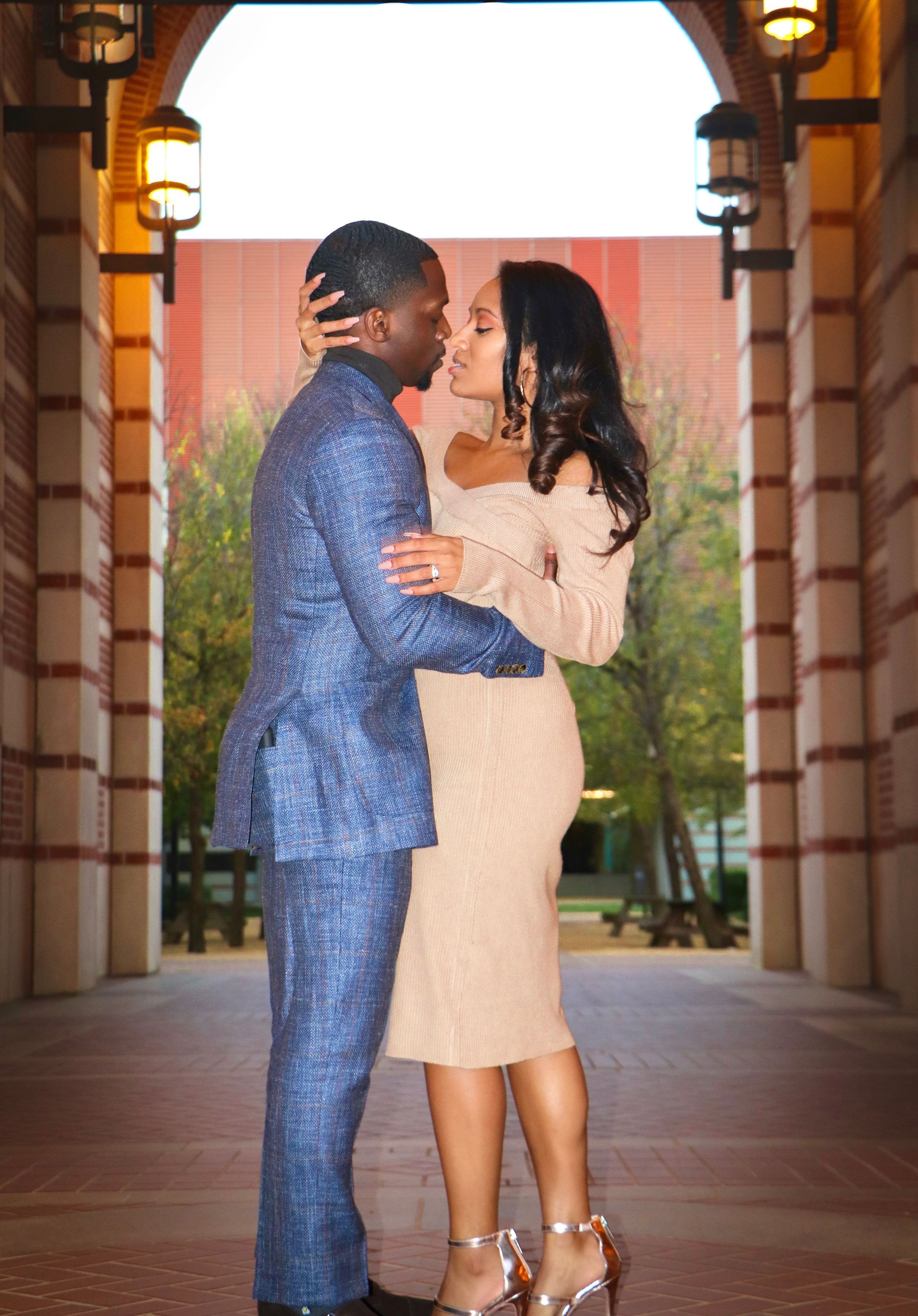 Romantic portrait of couple in formal wear sharing intimate moment under arched colonnade.