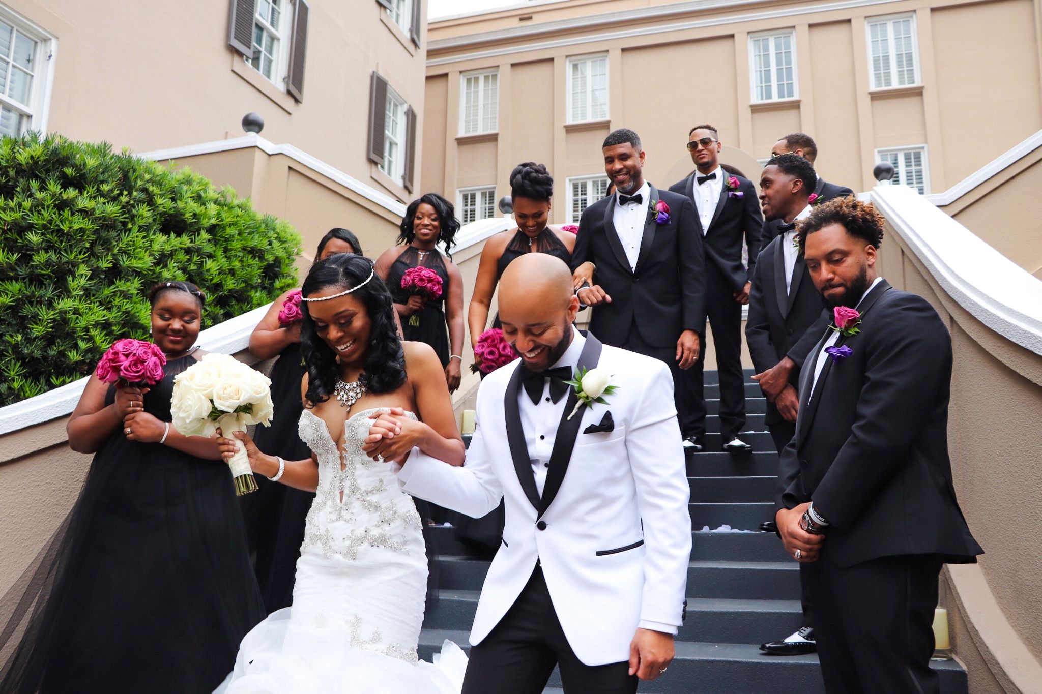 Wedding party in formal attire poses joyfully on outdoor stone steps.