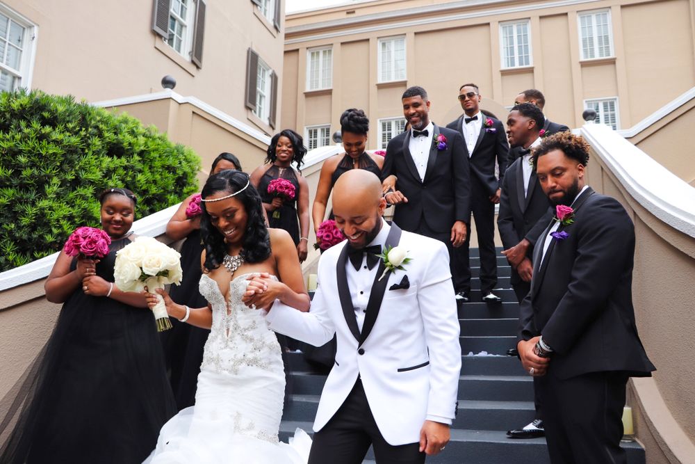 Wedding party in formal attire poses joyfully on outdoor stone steps.