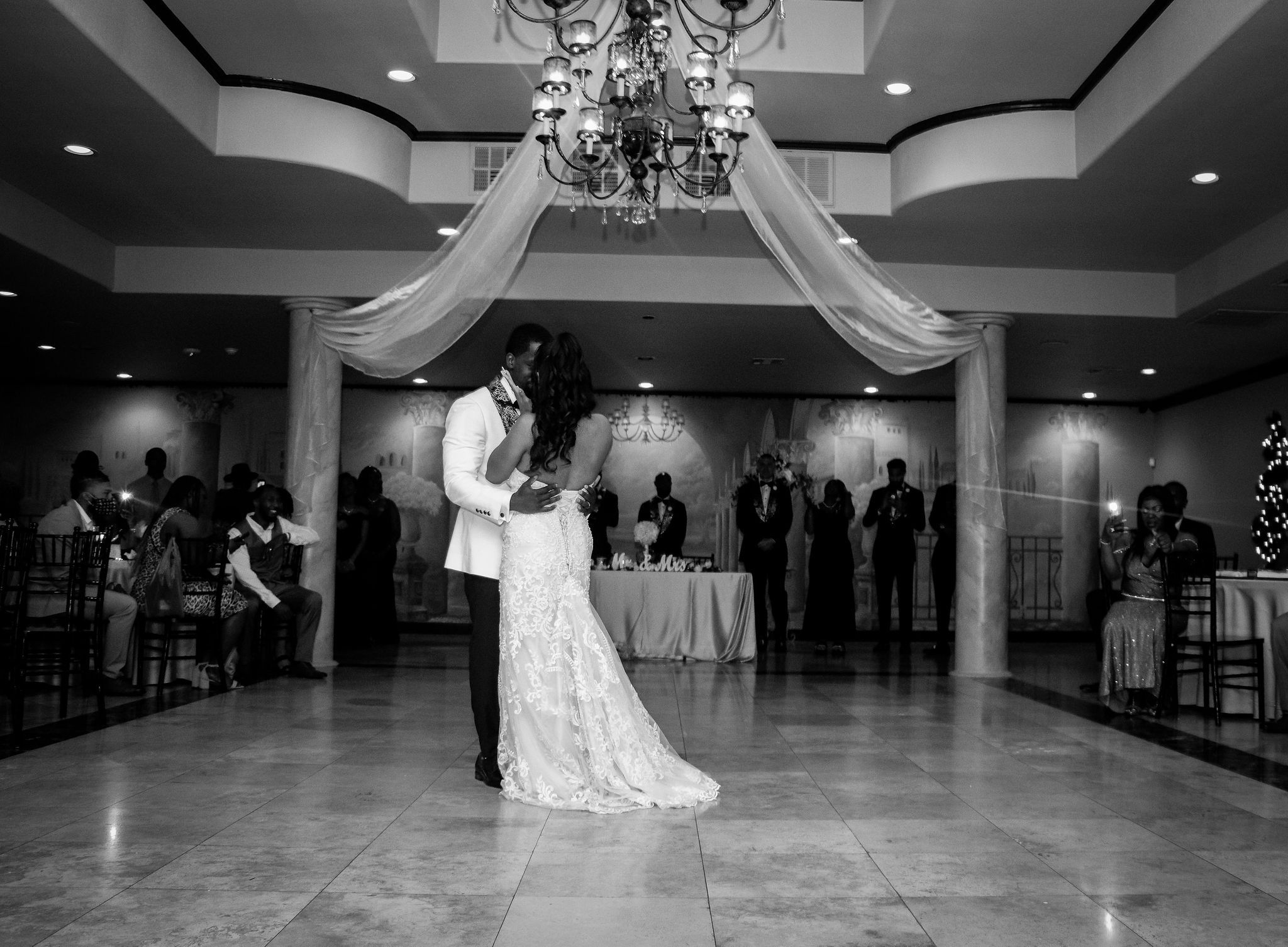 Black and white reception photo of couple's first dance under elegant ballroom decor.