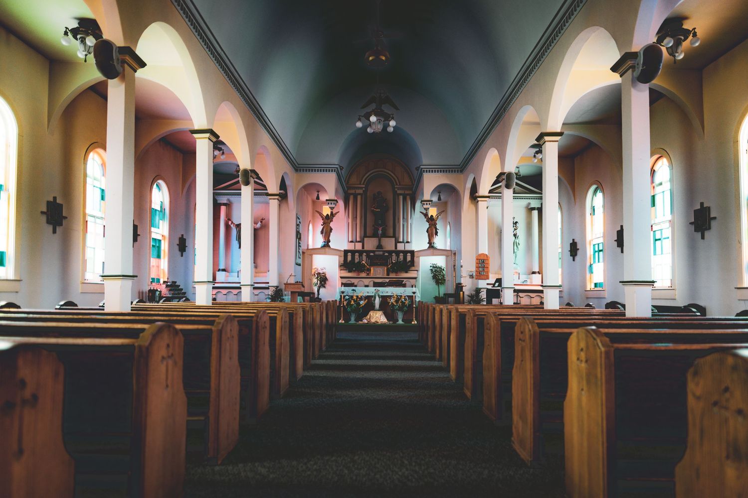 Interior panorama of an empty church sanctuary with wooden pews and arched ceilings.