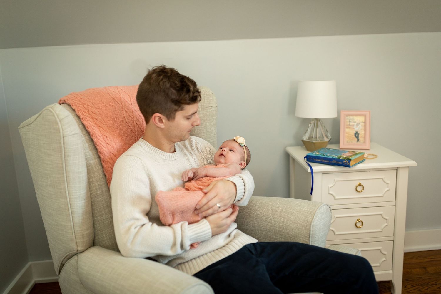 Peaceful nursery setting with white armchair and soft coral accents.