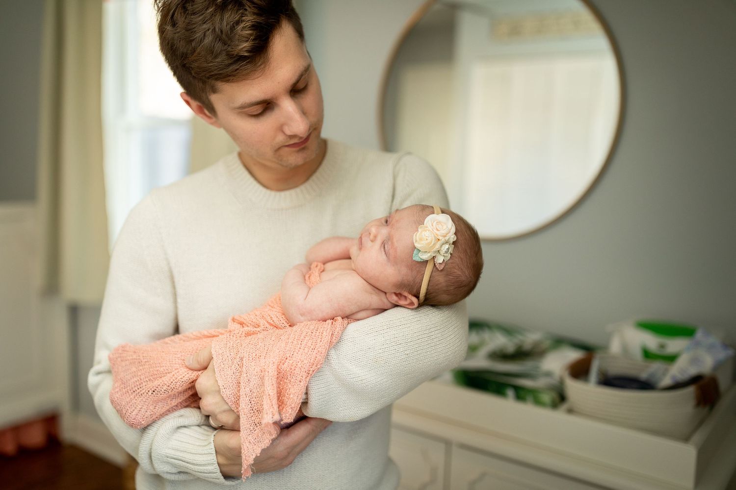 A tender moment as a caregiver cradles a newborn wearing a peachy-colored outfit in a softly lit room.
