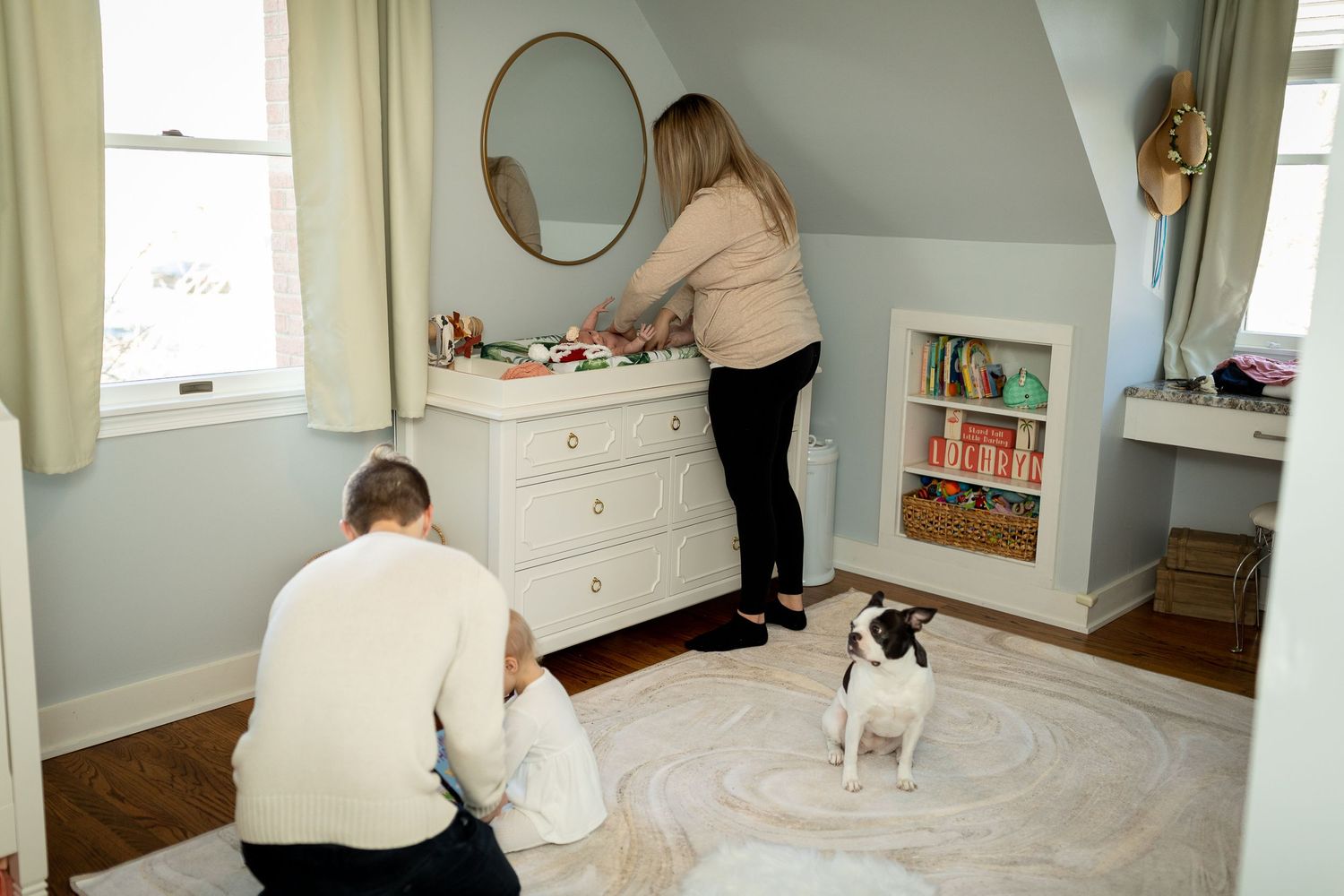 Panoramic view of nursery showing white furniture, gray walls, and oval mirror decor.