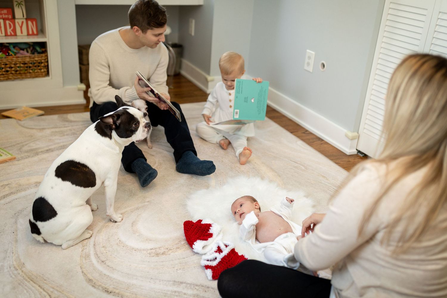 A family relaxes on a cream carpet with their black and white dog while spending time with their baby.