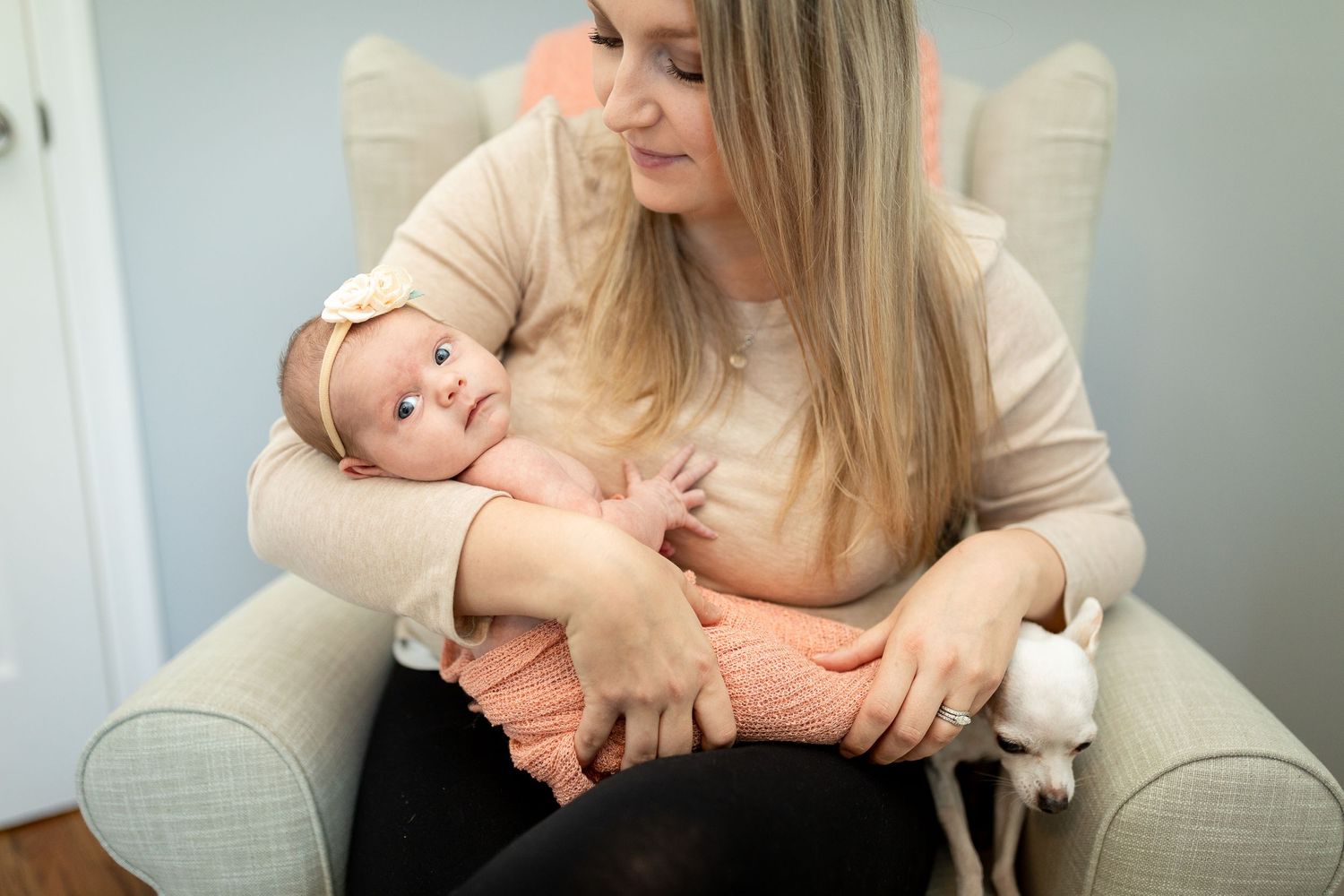 Parent cuddles with baby in cream colored armchair.
