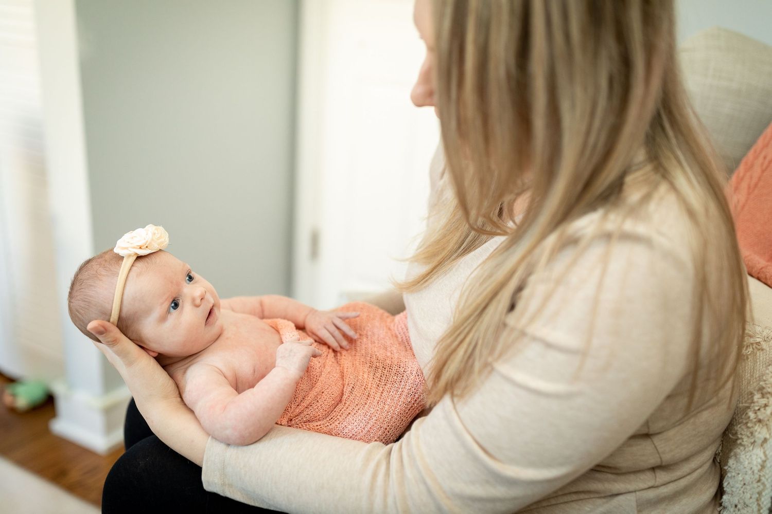 Baby in coral-colored outfit lying on soft fabric while being held.