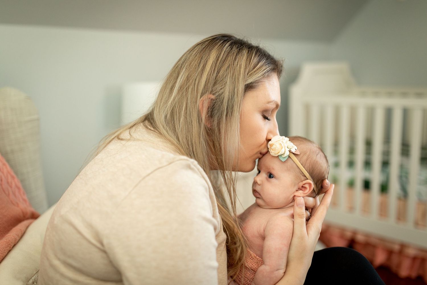 Nurturing moment between caregiver and baby near white crib.