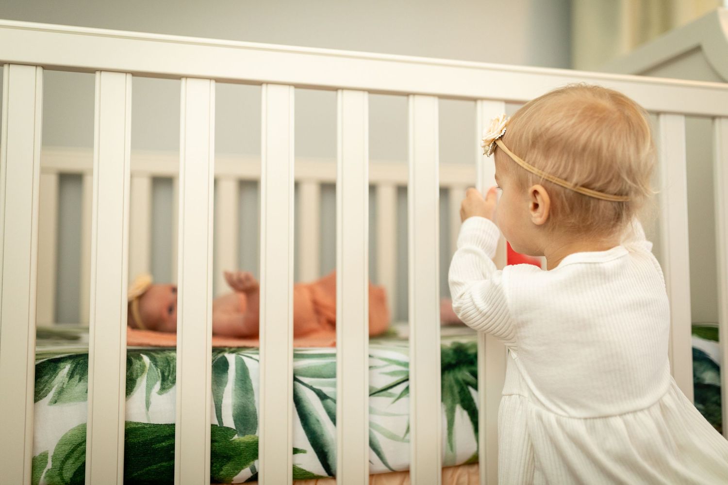 White crib with tropical leaf pattern visible in nursery setting.