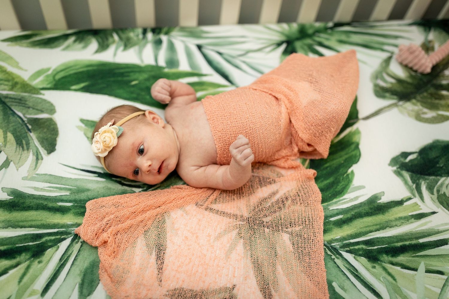 Baby lying on tropical leaf print bedding with peach-colored accessories.
