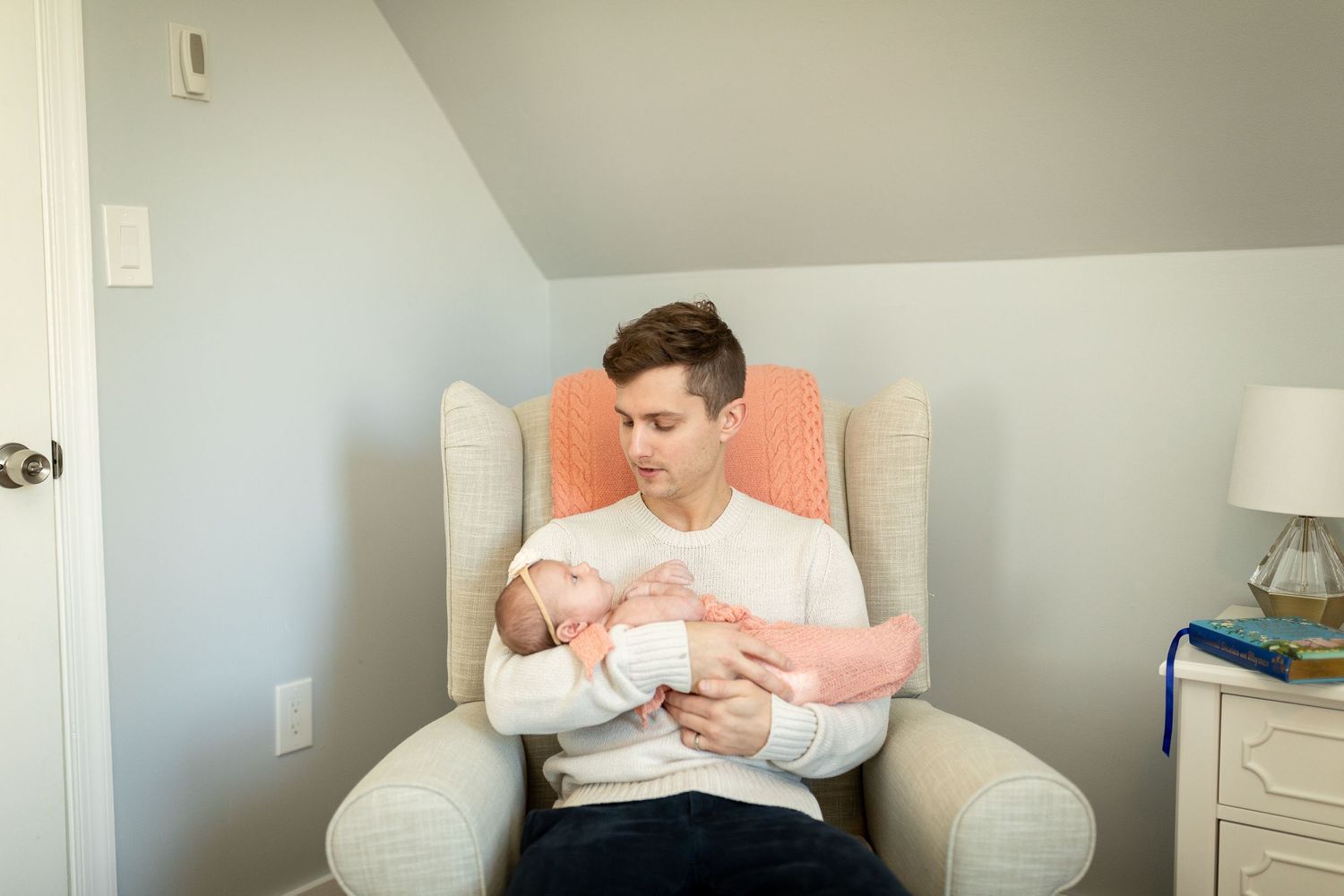 Cozy reading nook in nursery featuring white armchair and coral accent pillow.