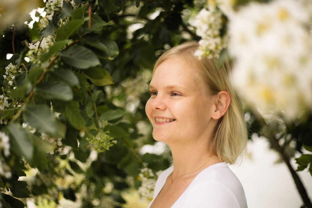 Outdoor portrait with white flowering branches and green leaves showing a gentle smile.