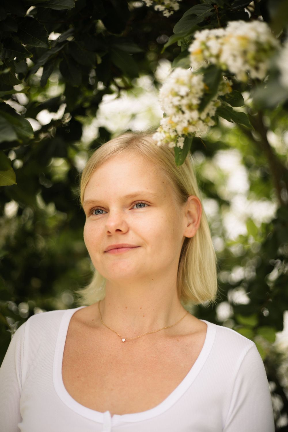 Close up portrait in natural lighting with white flowers and foliage in background.
