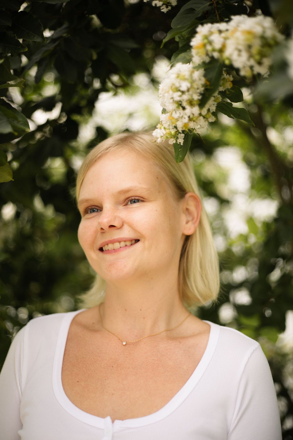 Cheerful portrait outdoors with blooming white flowers and green leaves in soft lighting.