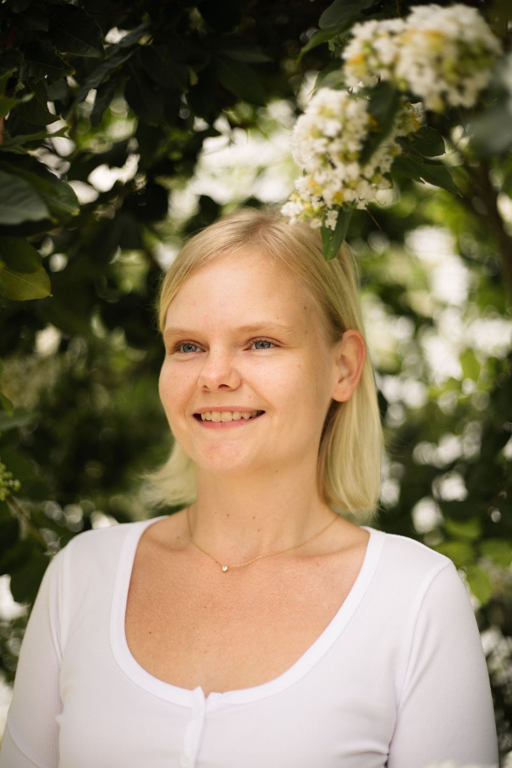 Natural outdoor portrait with white blooming flowers and green foliage framing the shot.