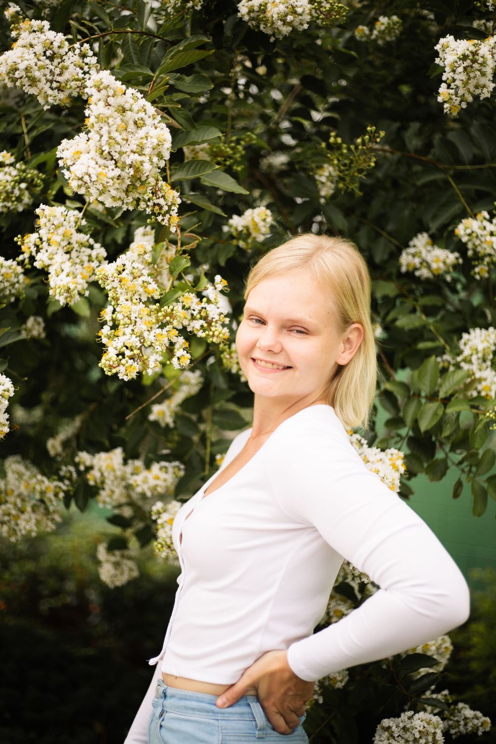 Candid portrait in white sweater against flowering bush background.
