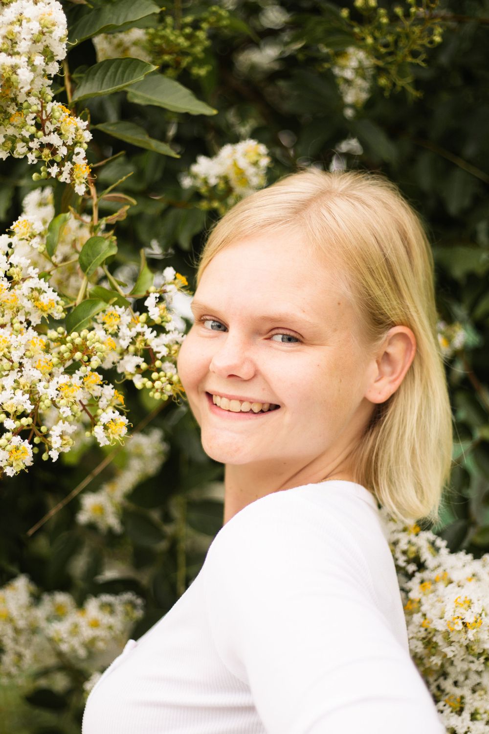 Portrait against green foliage with white blooming flowers in natural lighting.