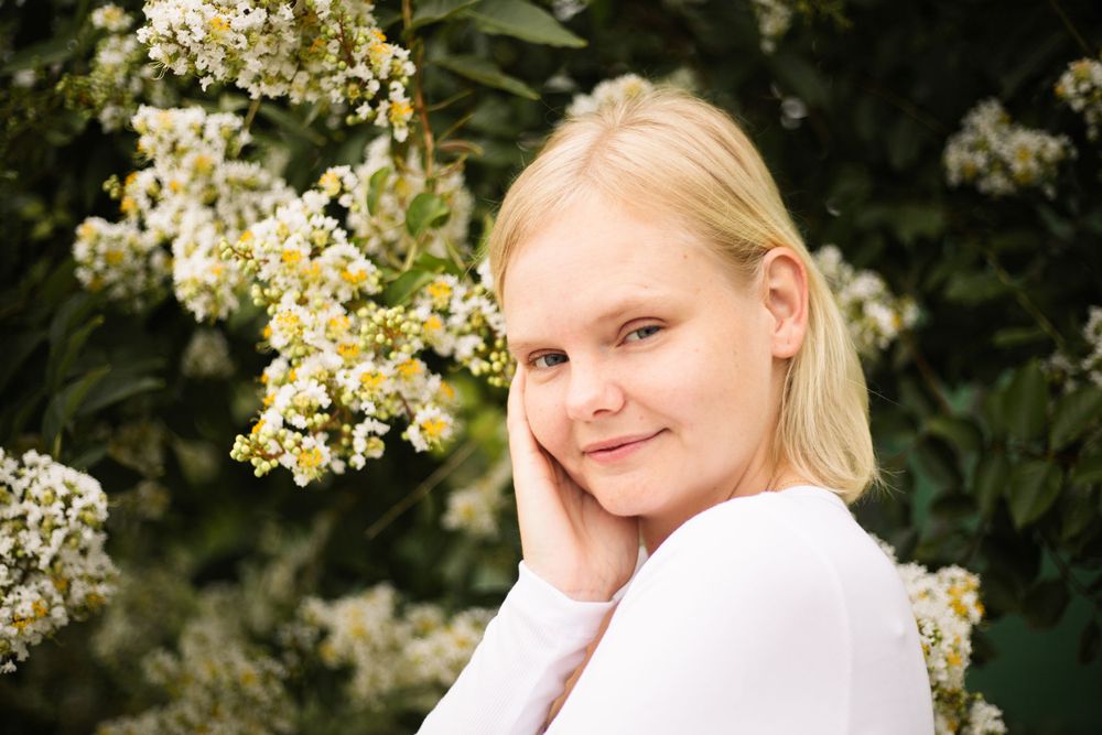 Casual outdoor portrait with white flowers and green foliage in background.