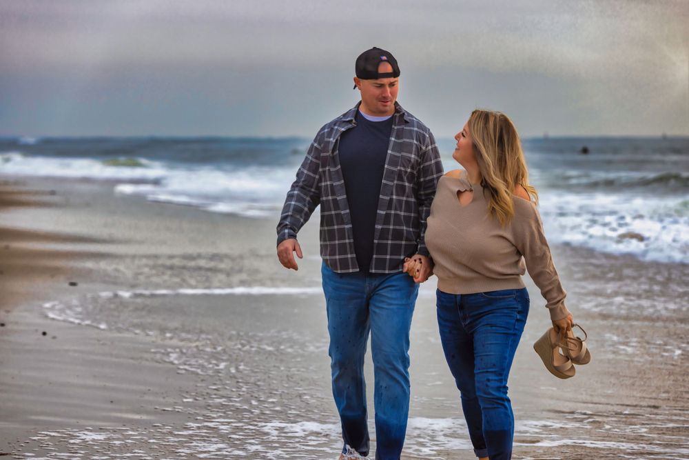 Couple walking hand in hand along misty beach shore at sunset.