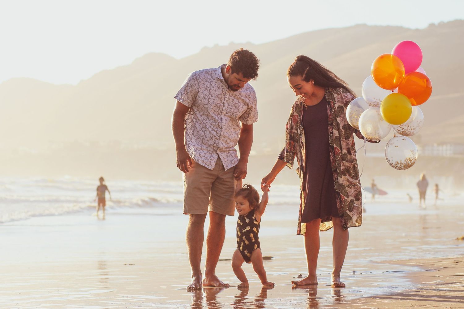 Family with balloons walks on beach in Pismo Beach