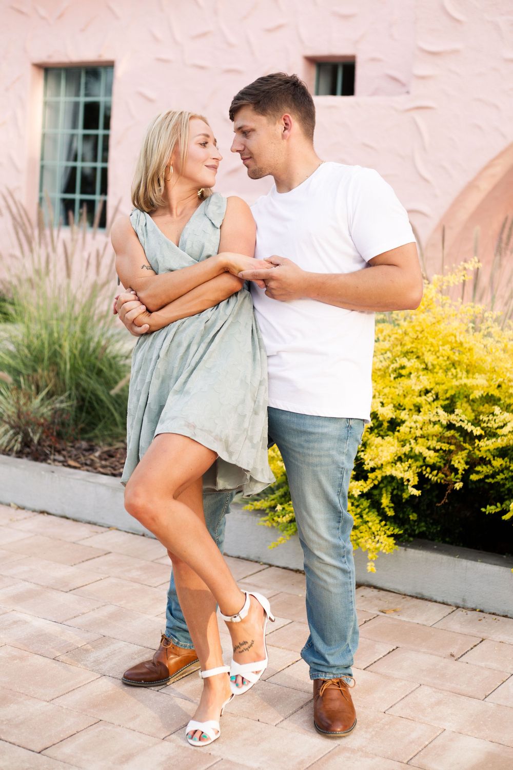 A couple shares a romantic moment on a patio with pink walls and yellow flowers.