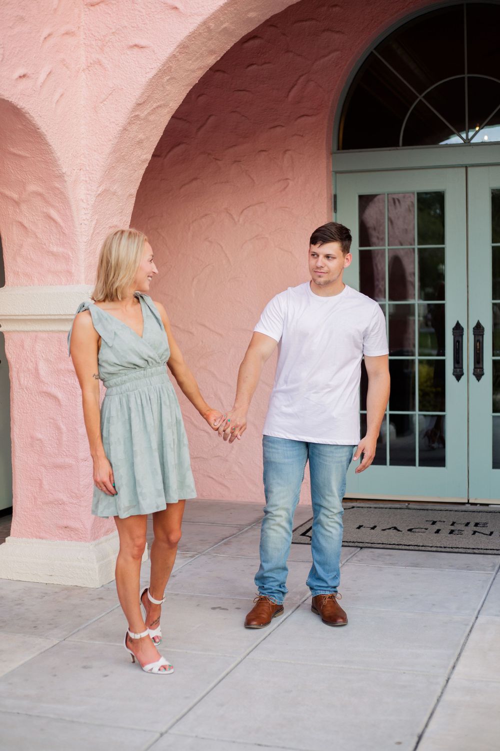 Couple holding hands while standing in front of glass doors with pink arches.