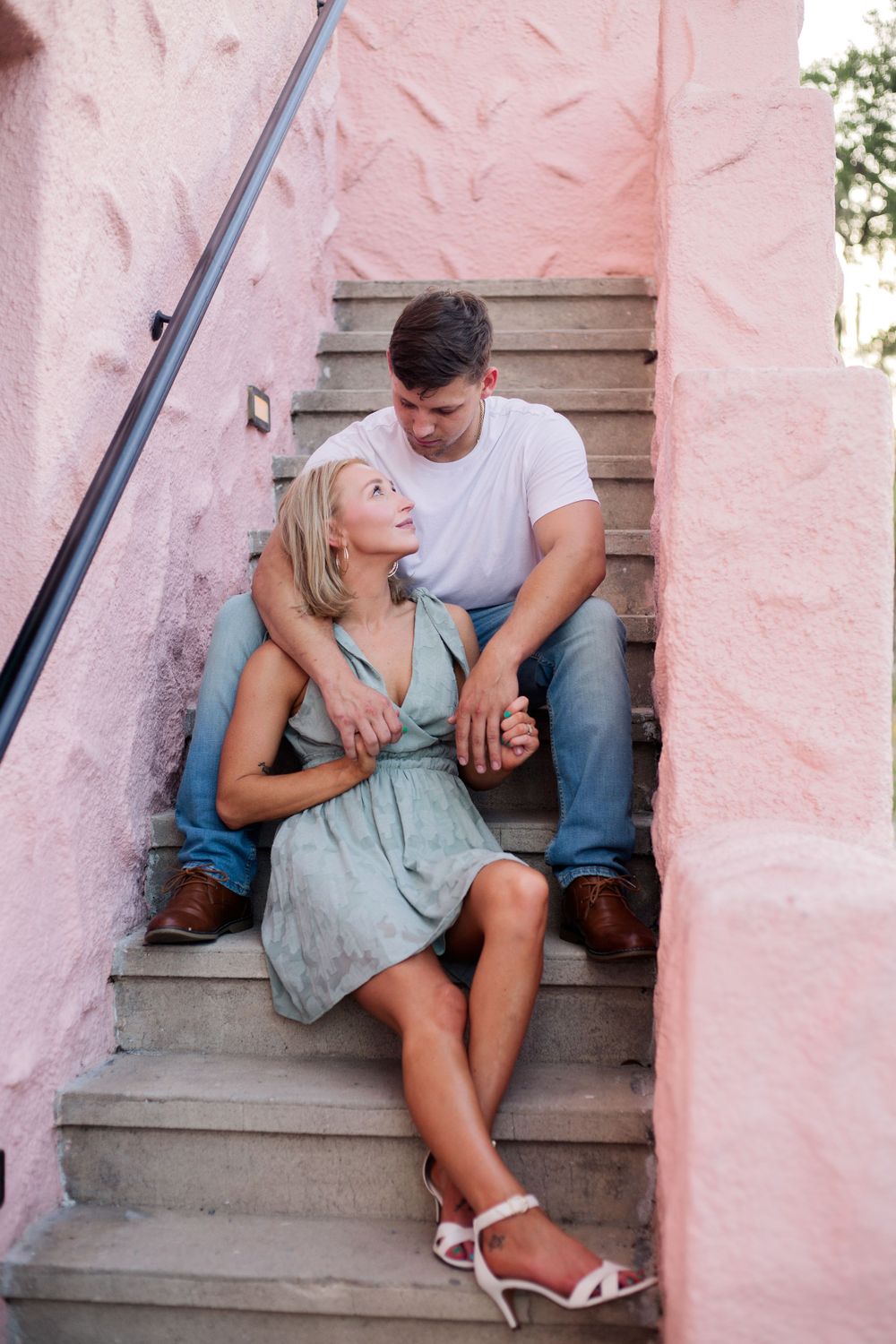 Couple sitting close together on concrete steps with pink walls.