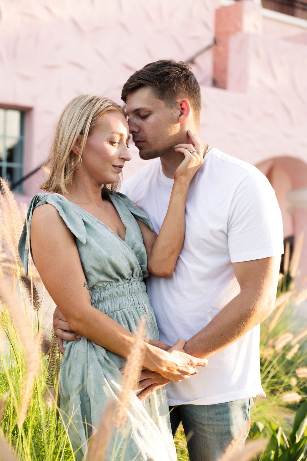 Couple sharing an intimate moment in front of ornate pink architecture.