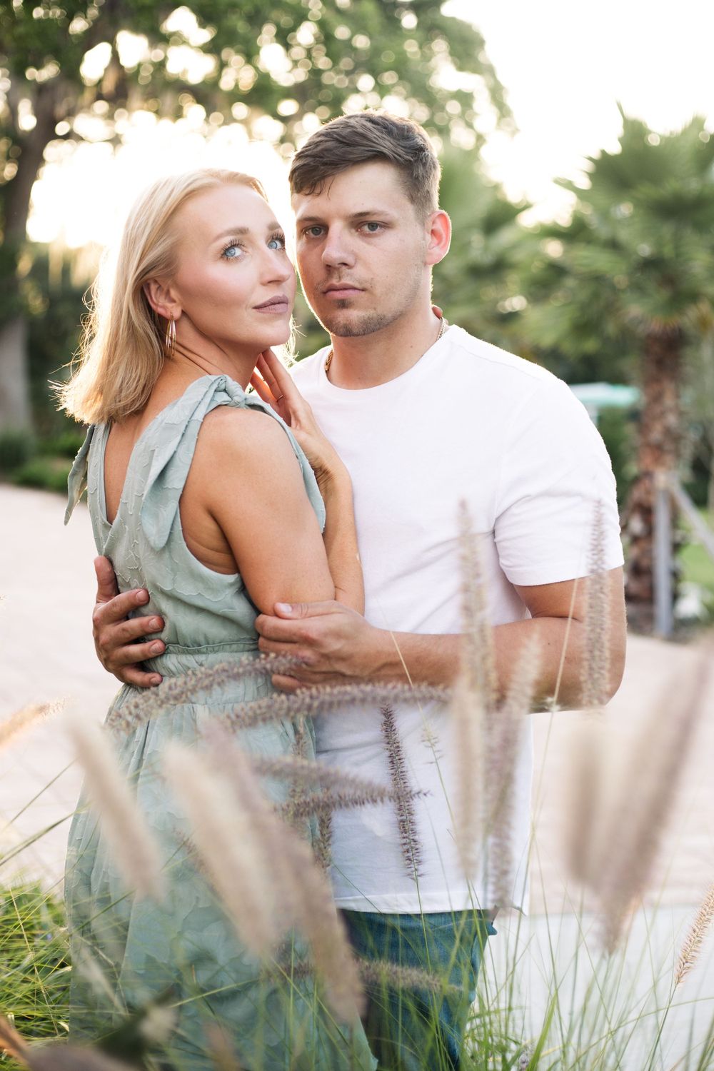 Couple in tender embrace among decorative grasses at golden hour.