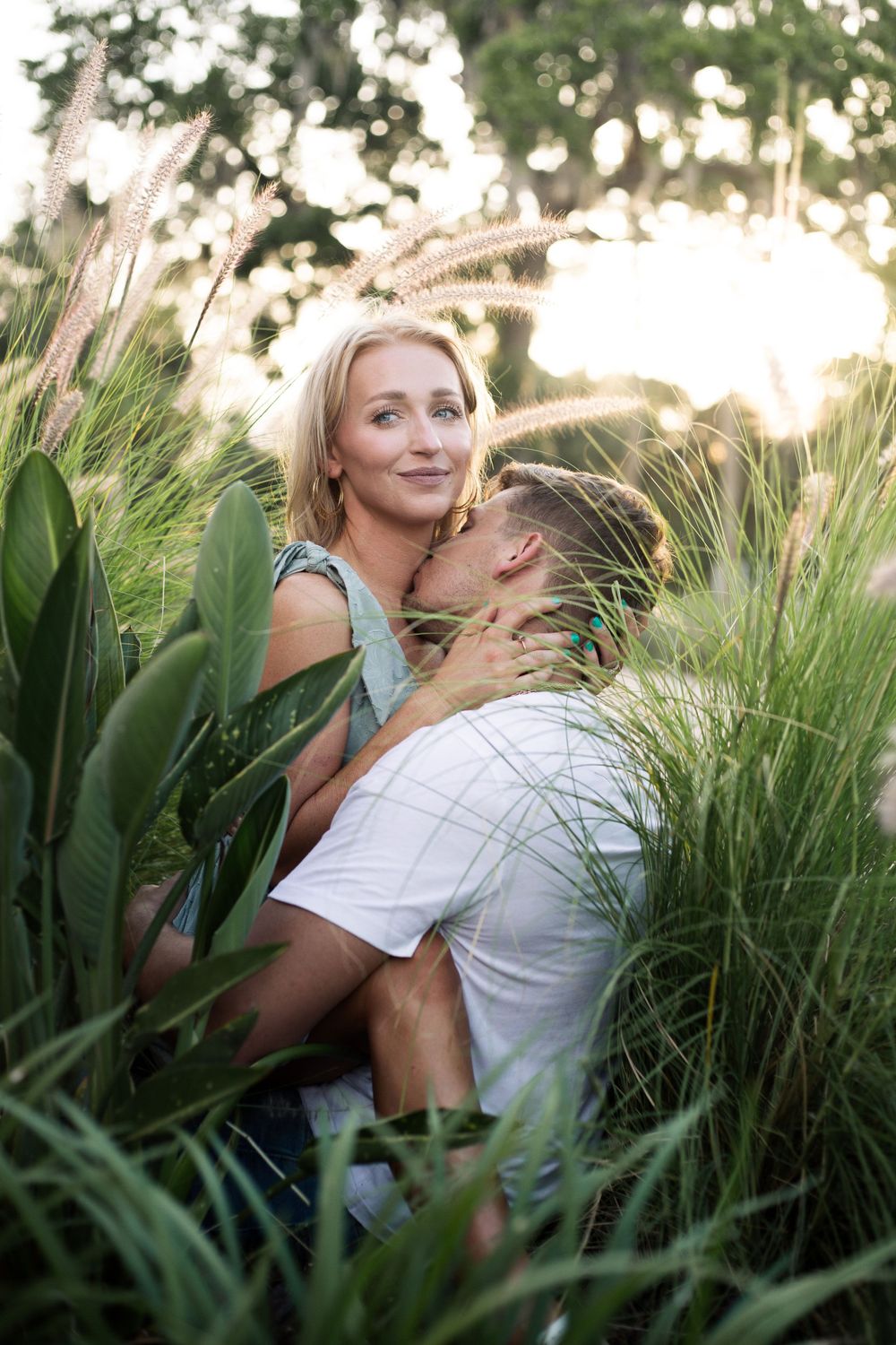 Intimate couple moment captured in tall grass during golden hour sunset.