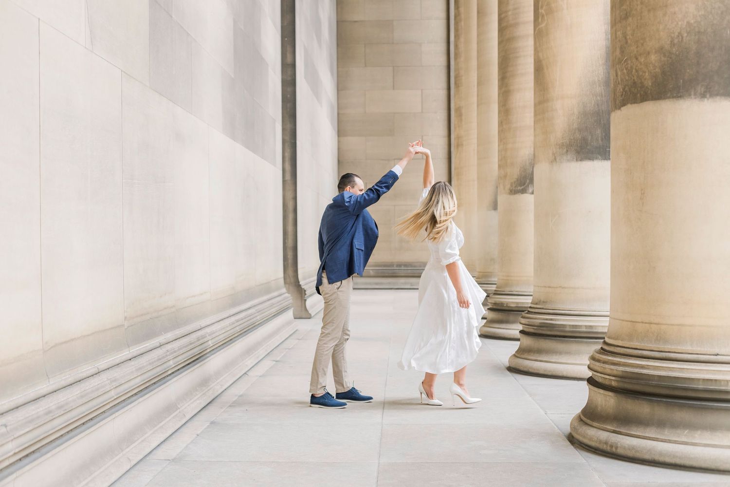 A couple dancing together in an elegant architectural setting with classical columns and natural lighting.