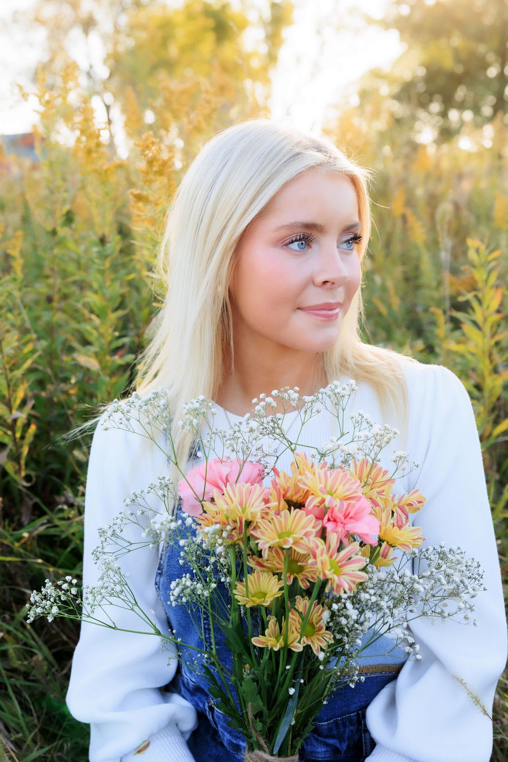 Outdoor portrait with a bouquet of pink and yellow flowers against golden autumn foliage.