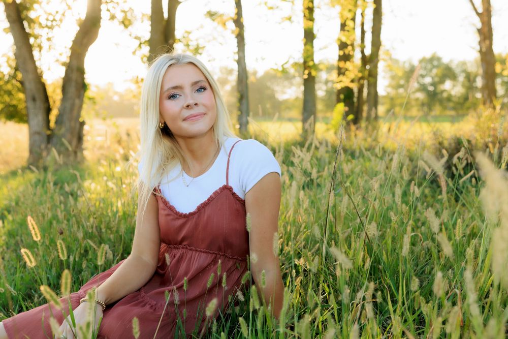 A portrait in a field shows someone in a burgundy dress relaxing among wildflowers at sunset.