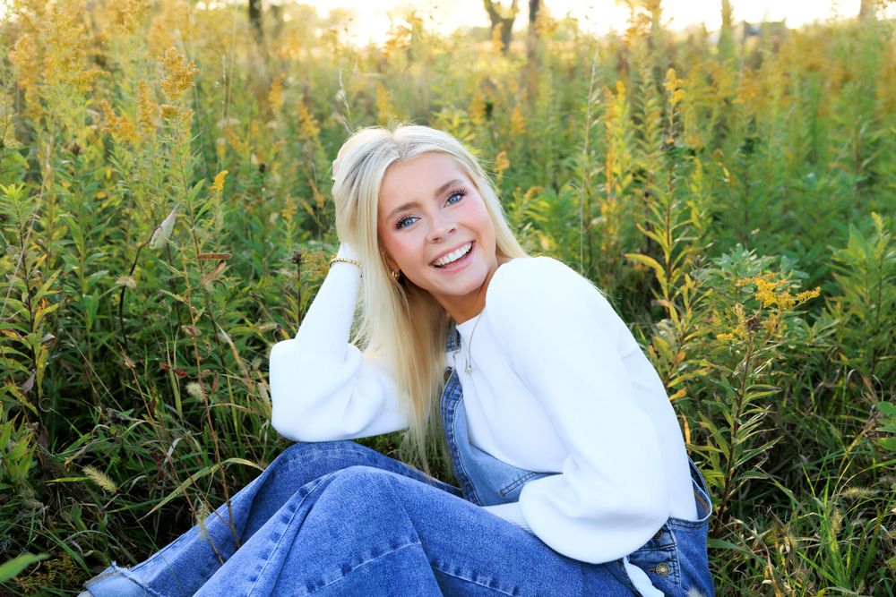 A person in a white sweater sits in tall grass during golden hour with a joyful expression.