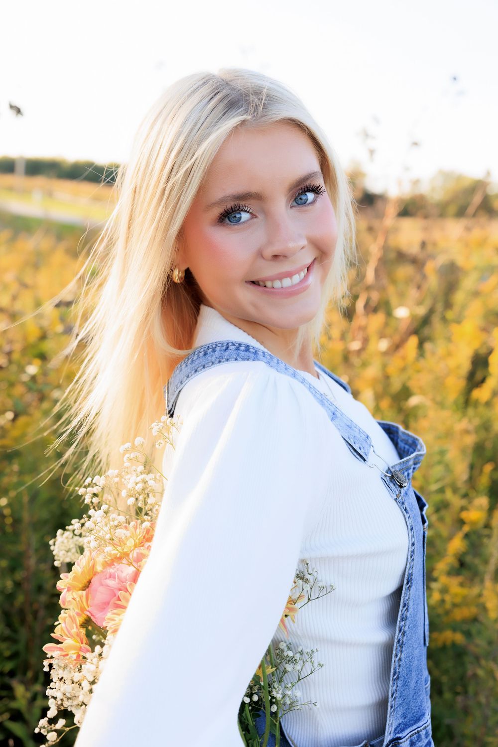 Side profile portrait in white sweater and denim against a field of yellow wildflowers.