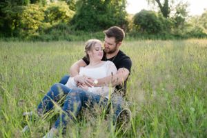 Romantic couple lounges together in a sunlit meadow with tall grass and wildflowers.