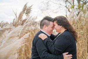 Couple embracing in tall autumn grass during golden hour.