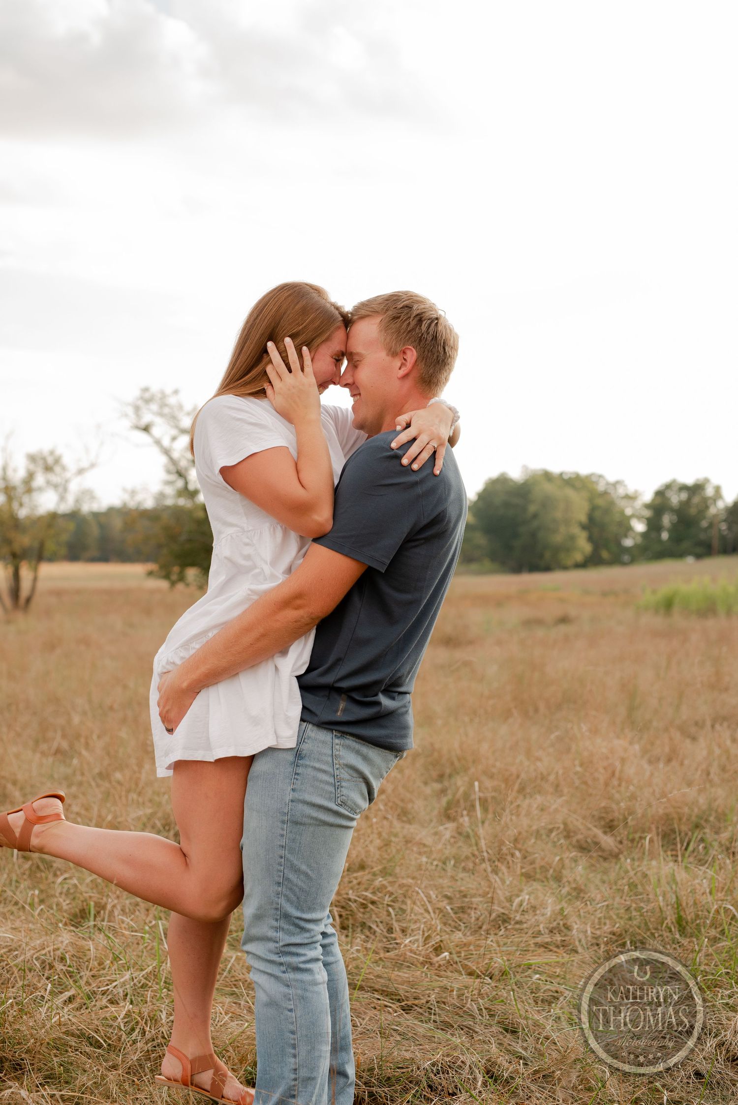 Romantic embrace between couple wearing casual attire in golden field.
