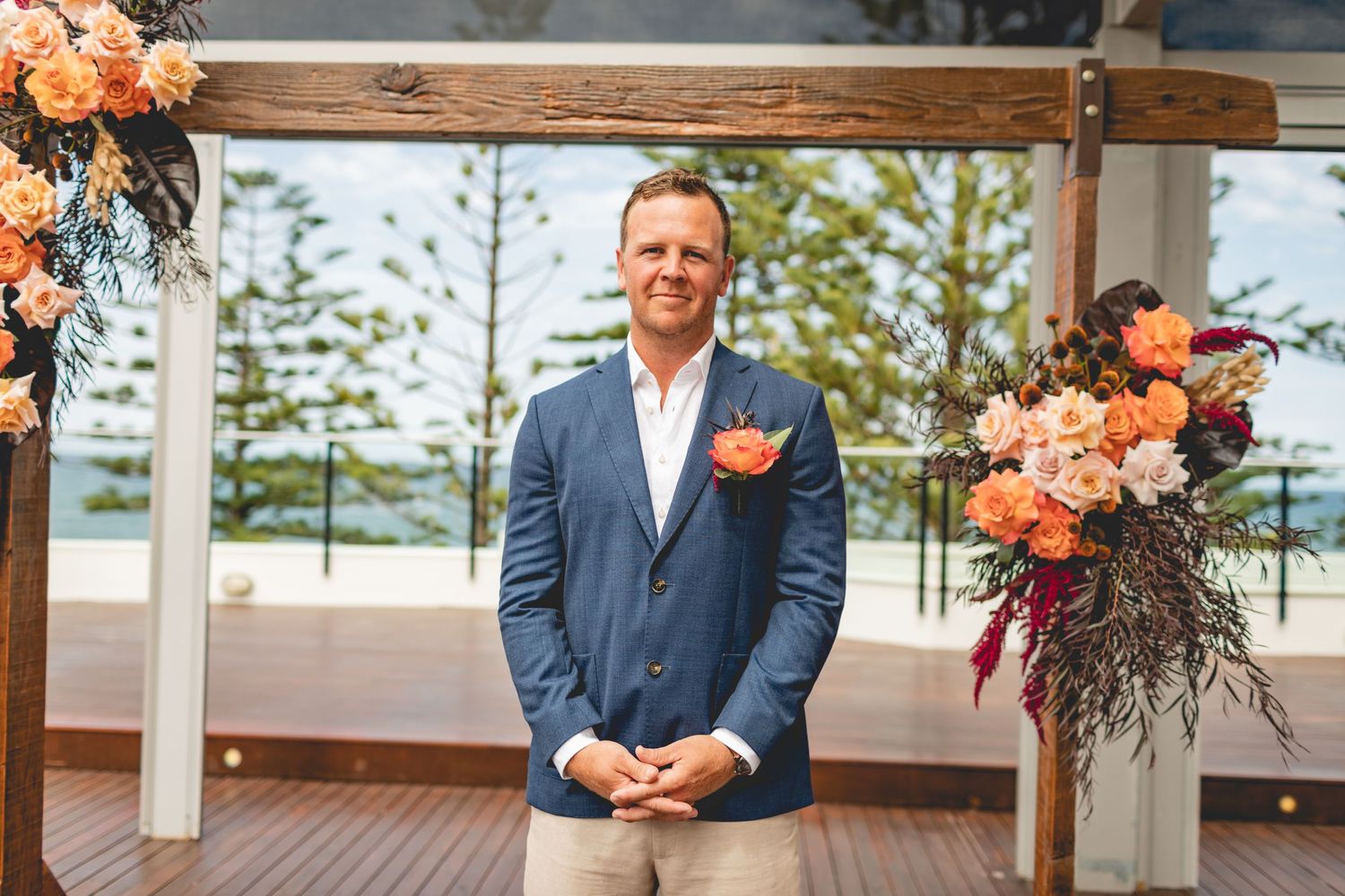 Decorated wedding ceremony arch with coral and peach floral arrangements on wooden deck.
