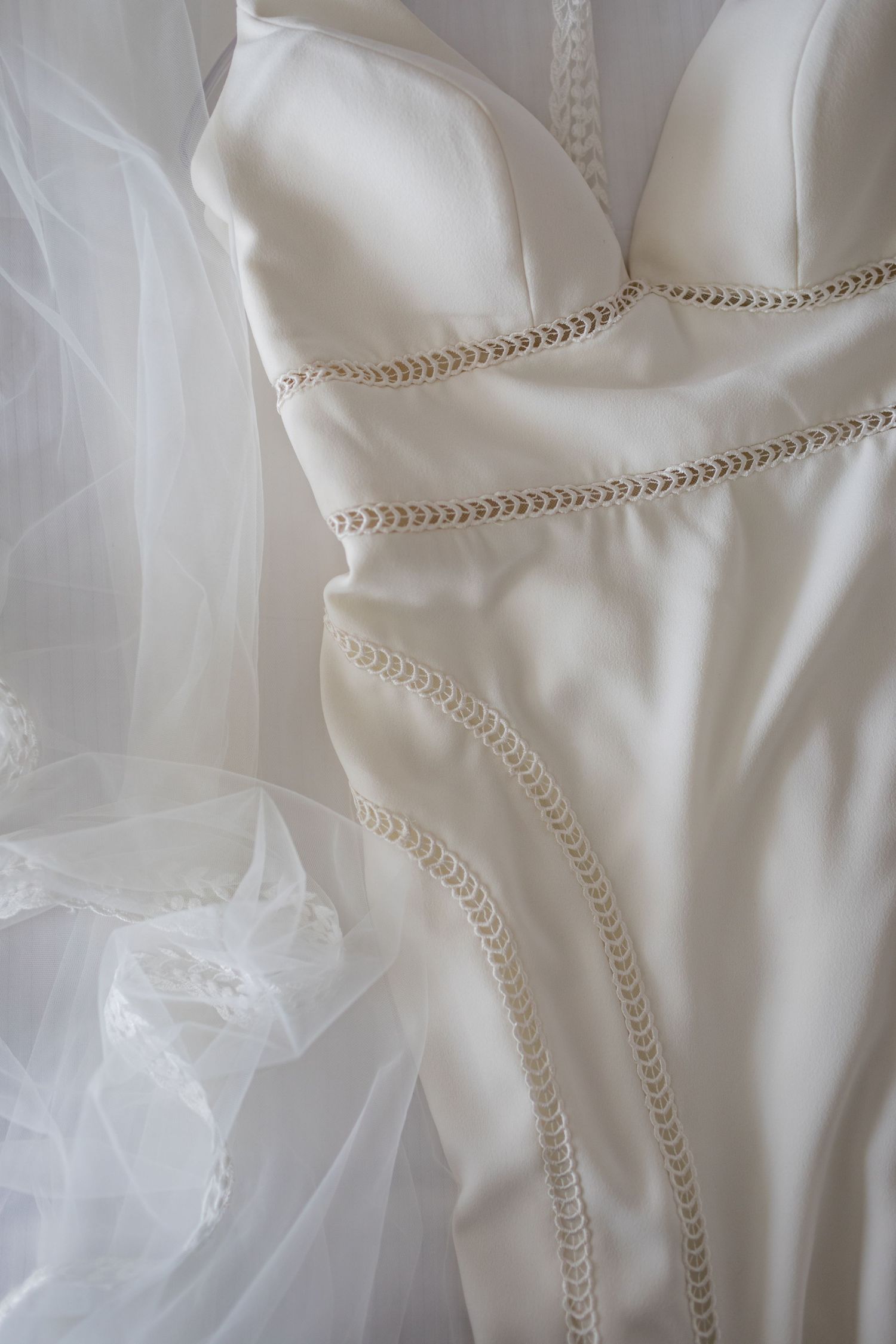 Close-up detail of white wedding dress bodice with delicate leaf embroidery and tulle fabric.