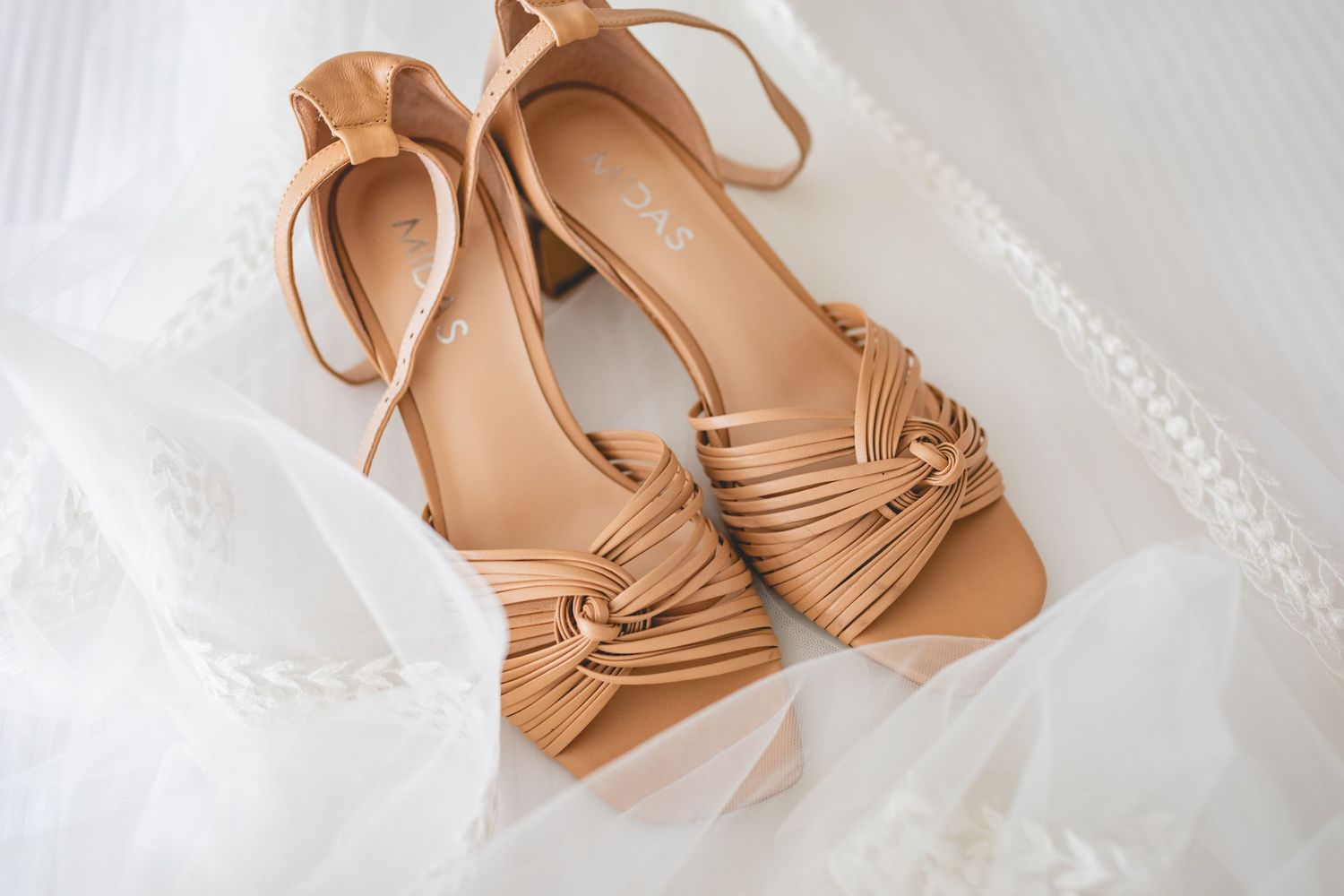 Tan leather strappy sandals with knot detail photographed on white fabric.