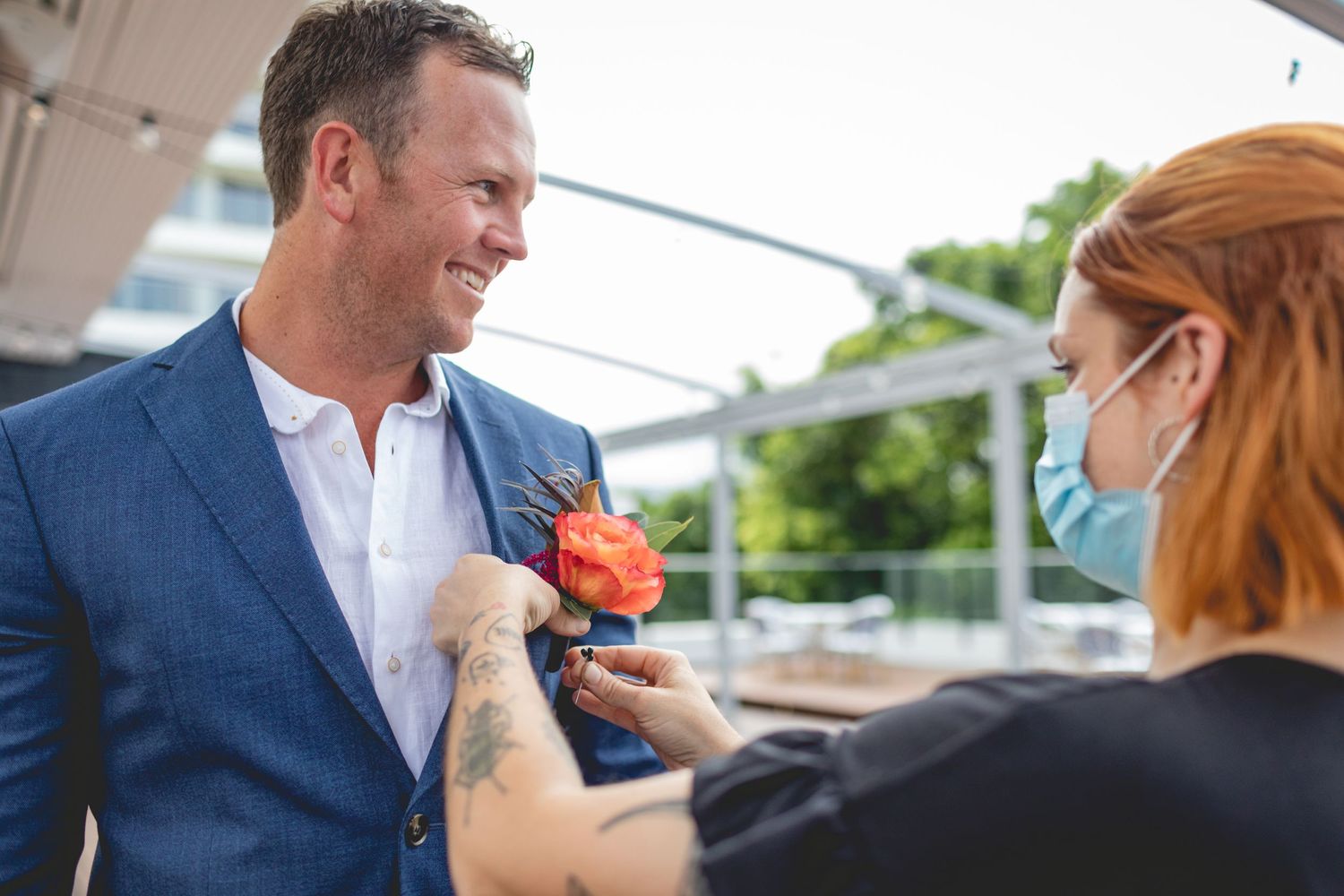 Wedding boutonniere being pinned on navy suit jacket outdoors.