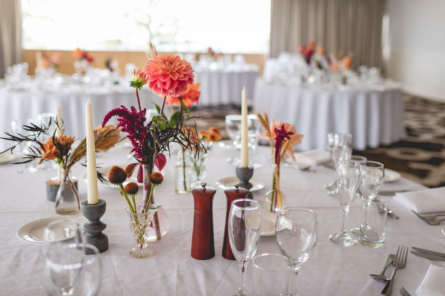 Wedding reception table setting with colorful floral centerpieces in mixed height vases.